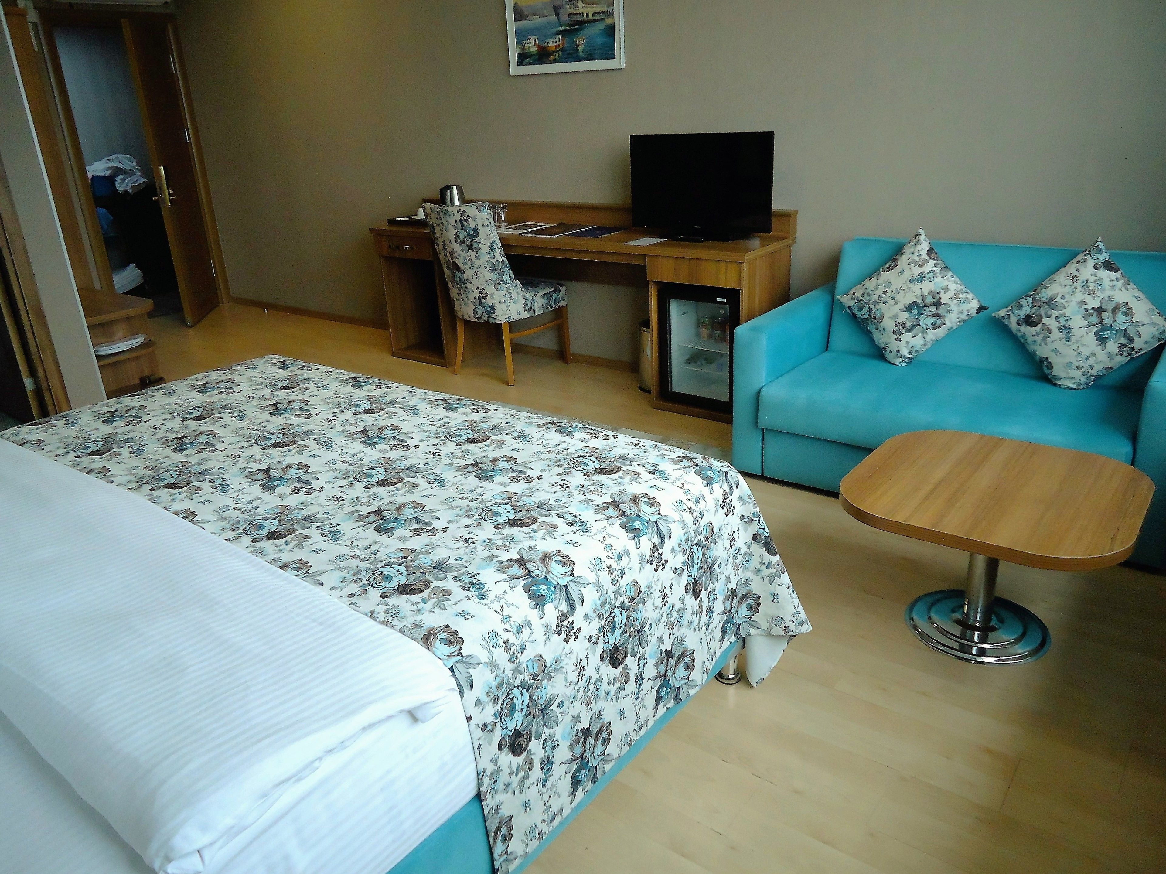 A hotel room with a bed, a desk with a computer, a small table, and a blue sofa with floral cushions.