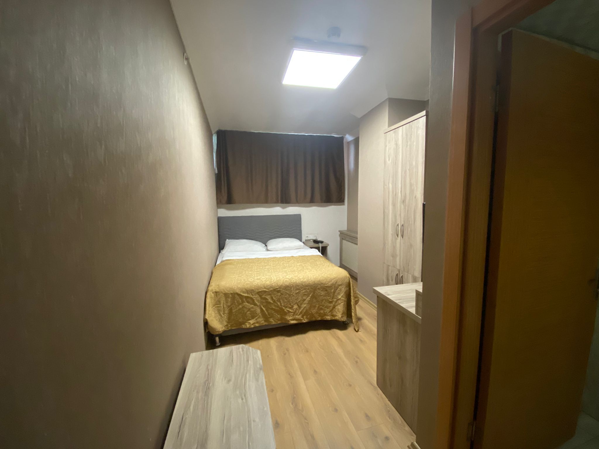 A small, narrow room with a bed, a wardrobe, and a desk.