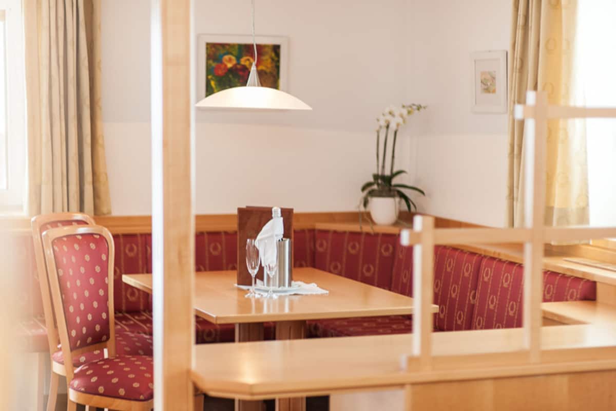 A dining area with wooden tables and red cushioned booths, a white pendant light, and a potted plant on the wall.