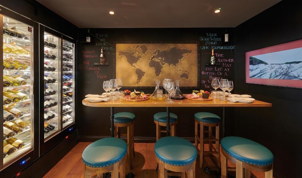 A bar area with a world map, wine glasses, and stools.
