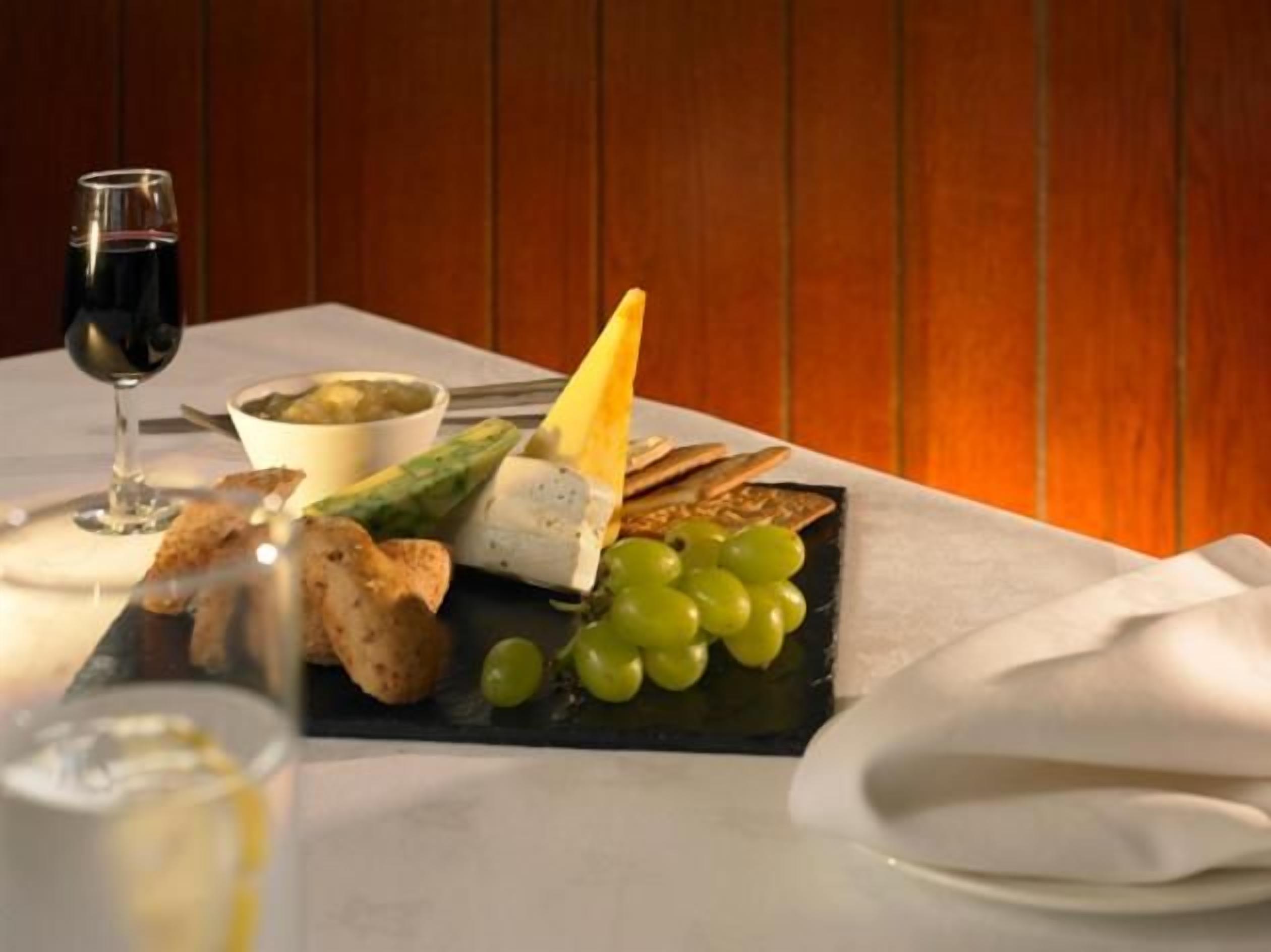 A dining table with a cheese platter, grapes, bread, and a glass of red wine.