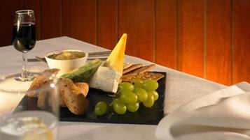 A dining table with a cheese platter, grapes, bread, and a glass of red wine.