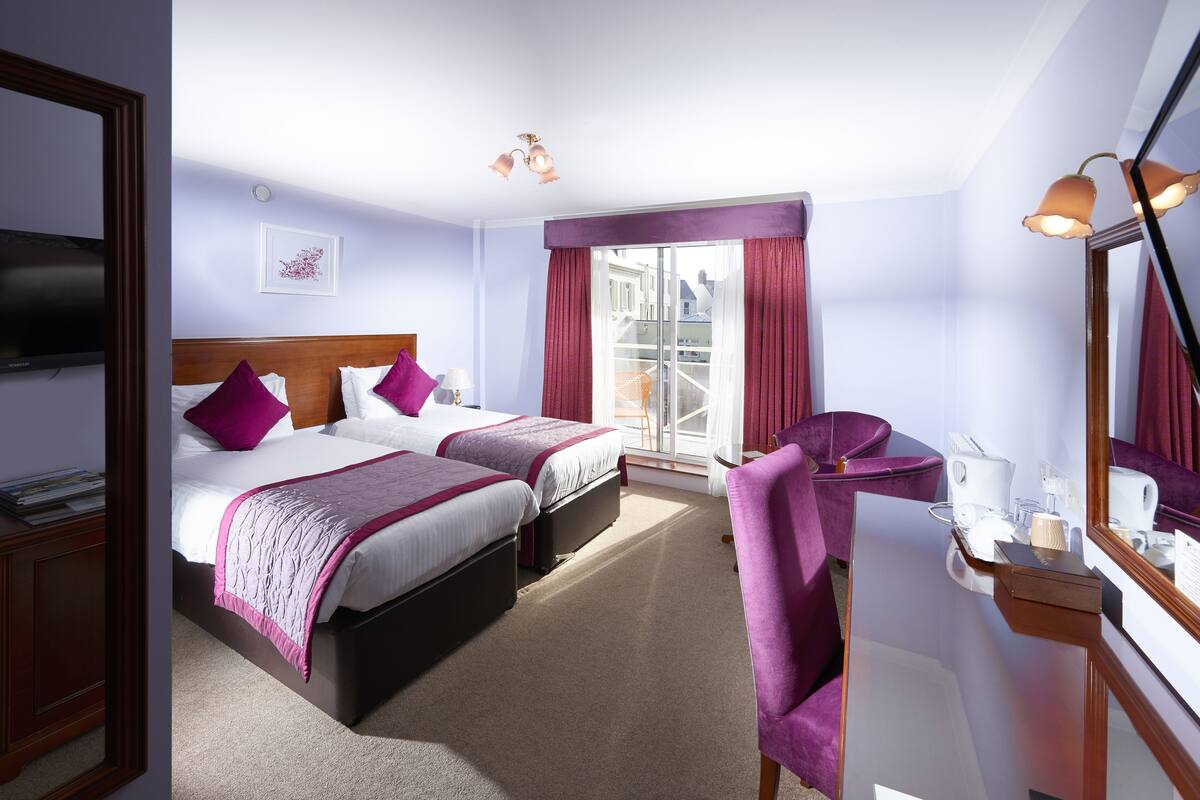 A hotel room with two beds, a sitting area with a chair, a desk with a mirror, and a television.
