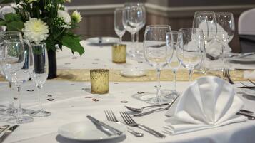 Mesa posta para um evento de jantar formal, com vários copos de vinho, pratos, talheres e um arranjo floral como centro.