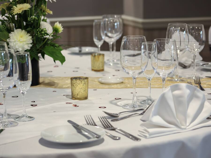 Mesa posta para um evento de jantar formal, com vários copos de vinho, pratos, talheres e um arranjo floral como centro.