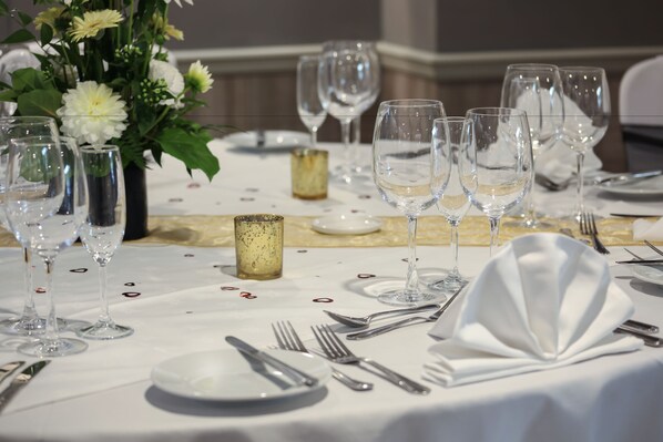 Una mesa dispuesta para un evento formal de cena, con varios vasos de vino, platos, cubiertos y un centro de mesa con flores.