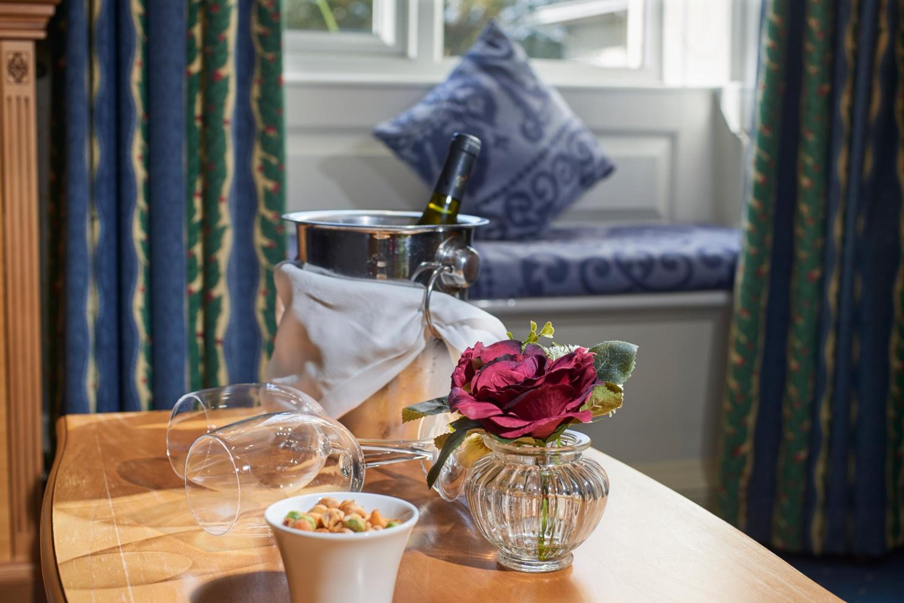 Une table en bois sur laquelle se trouvent une bouteille de vin, un verre, un bol de noix et un vase avec une fleur.
