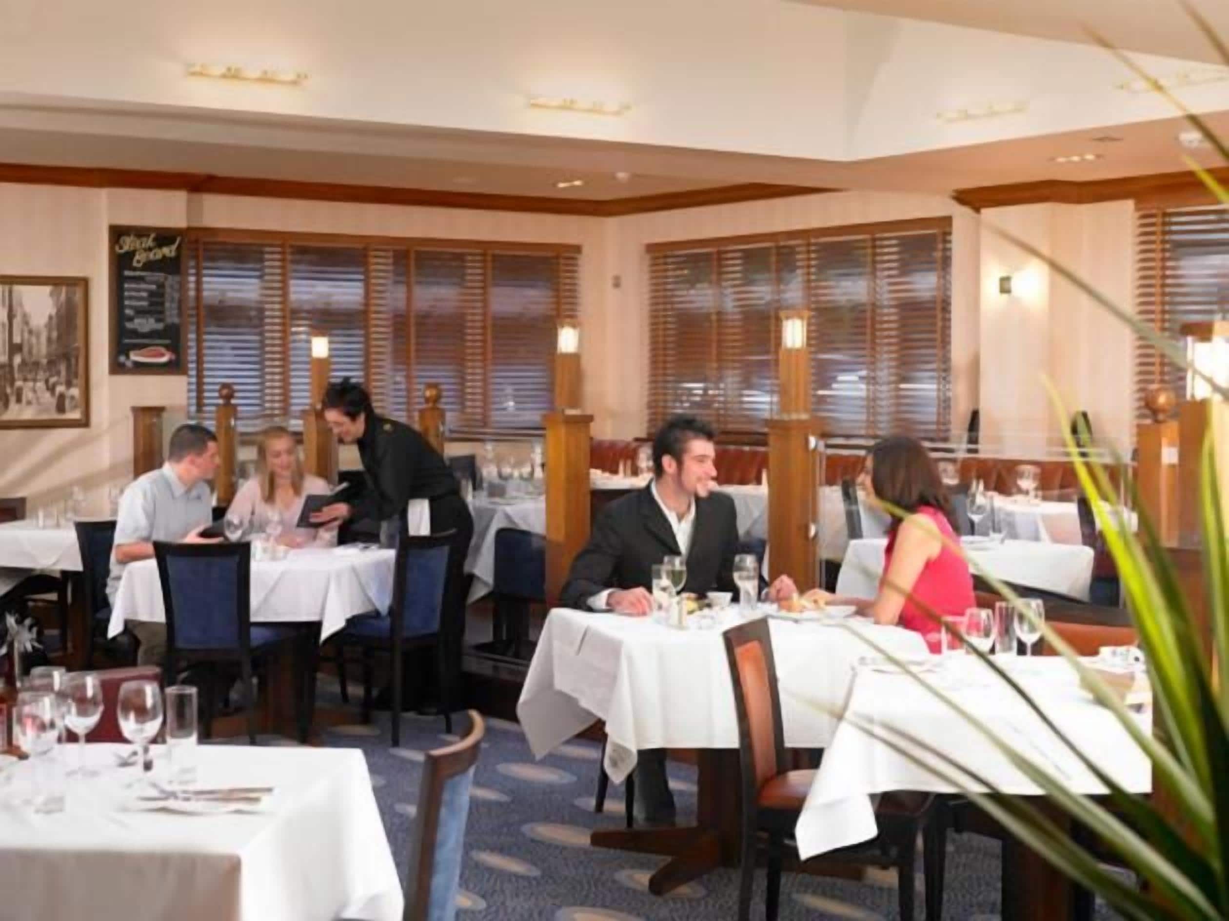 Un restaurante con mesas dispuestas para comer, un camarero atendiendo a los clientes y un menú en la pared.