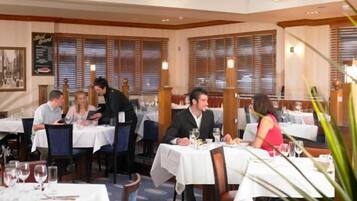 Un restaurante con mesas dispuestas para comer, un camarero atendiendo a los clientes y un menú en la pared.