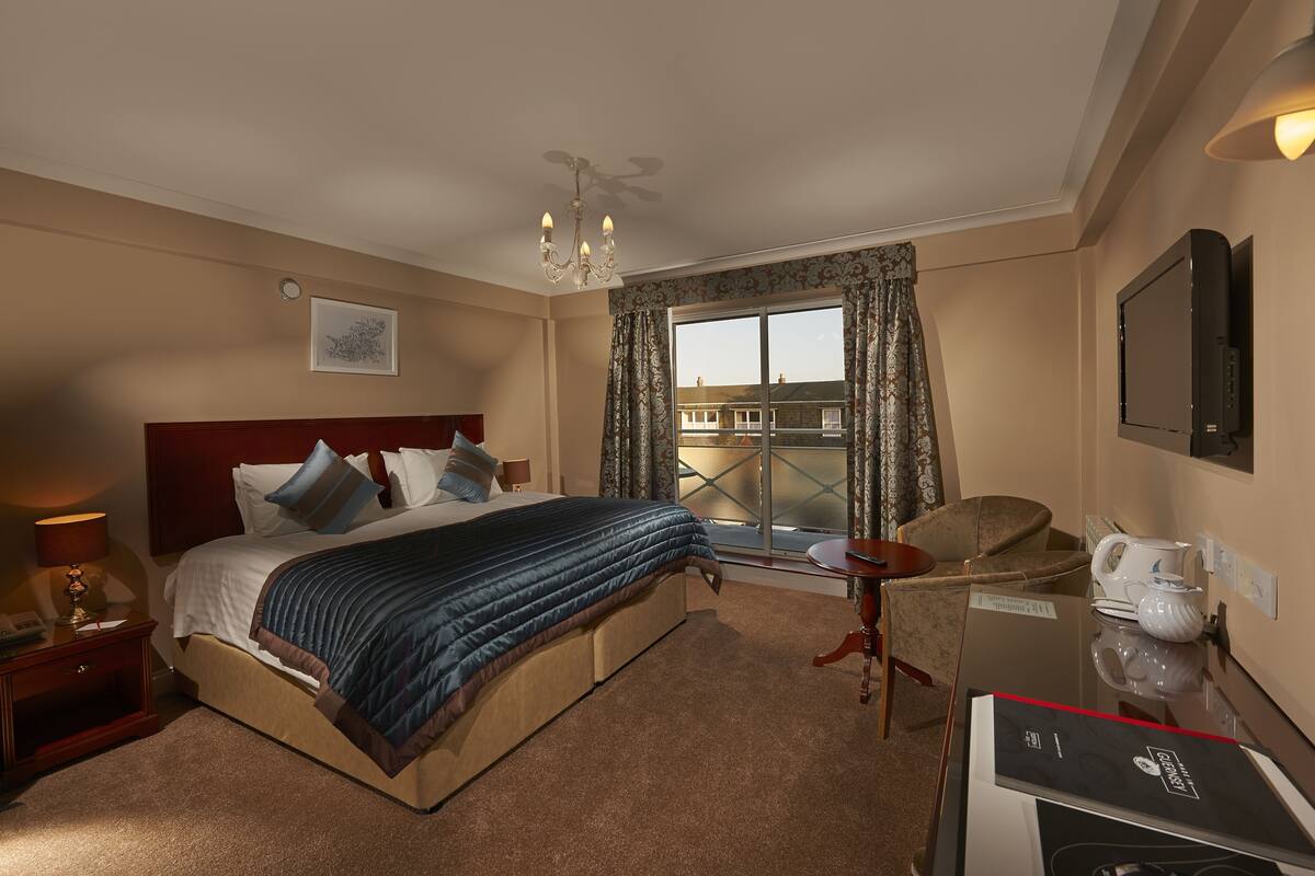 A hotel room with a large bed, a desk with a chair, a television, and a window with curtains.