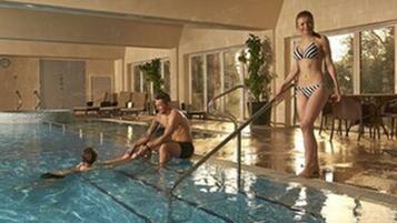 Una piscina interior amb aigua cristal·lina, una cadira de socorristes i una persona amb banyador.
