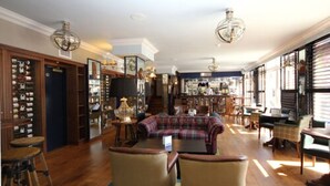 Una habitación amplia con un gran ventanal, un sofá a cuadros y una zona de bar con diversos objetos exhibidos.