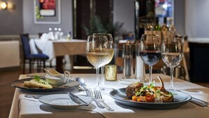Una mesa de comedor servida con platos de comida, copas de vino y cubiertos.