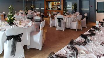 A banquet hall with round tables set for a formal event, each with white tablecloths and chairs adorned with black sashes.
