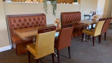 A dining area with a wooden table and cushioned chairs, a bench, and a clock on the wall.