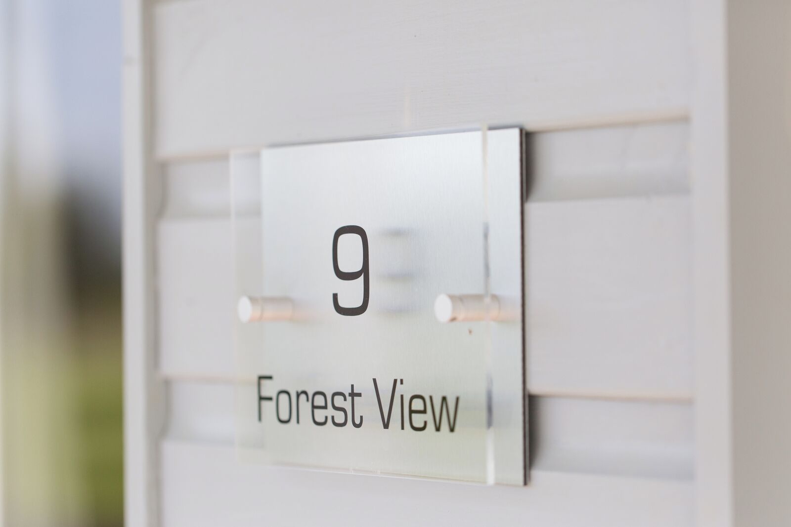 Een huisnummerbord met het getal 9 en de tekst 'Forest View' op een witte muur.