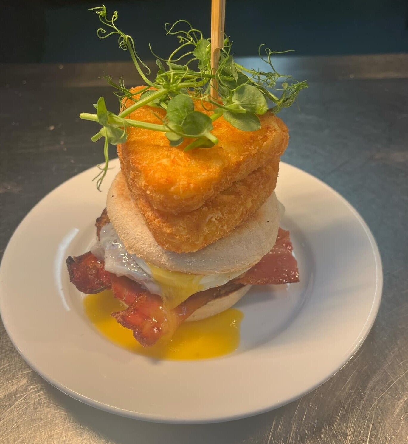 A breakfast dish with a fried egg, bacon, and a piece of bread, garnished with greens.