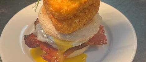 Plato de desayuno con un huevo frito, tocino y una rebanada de pan, adornado con vegetales.