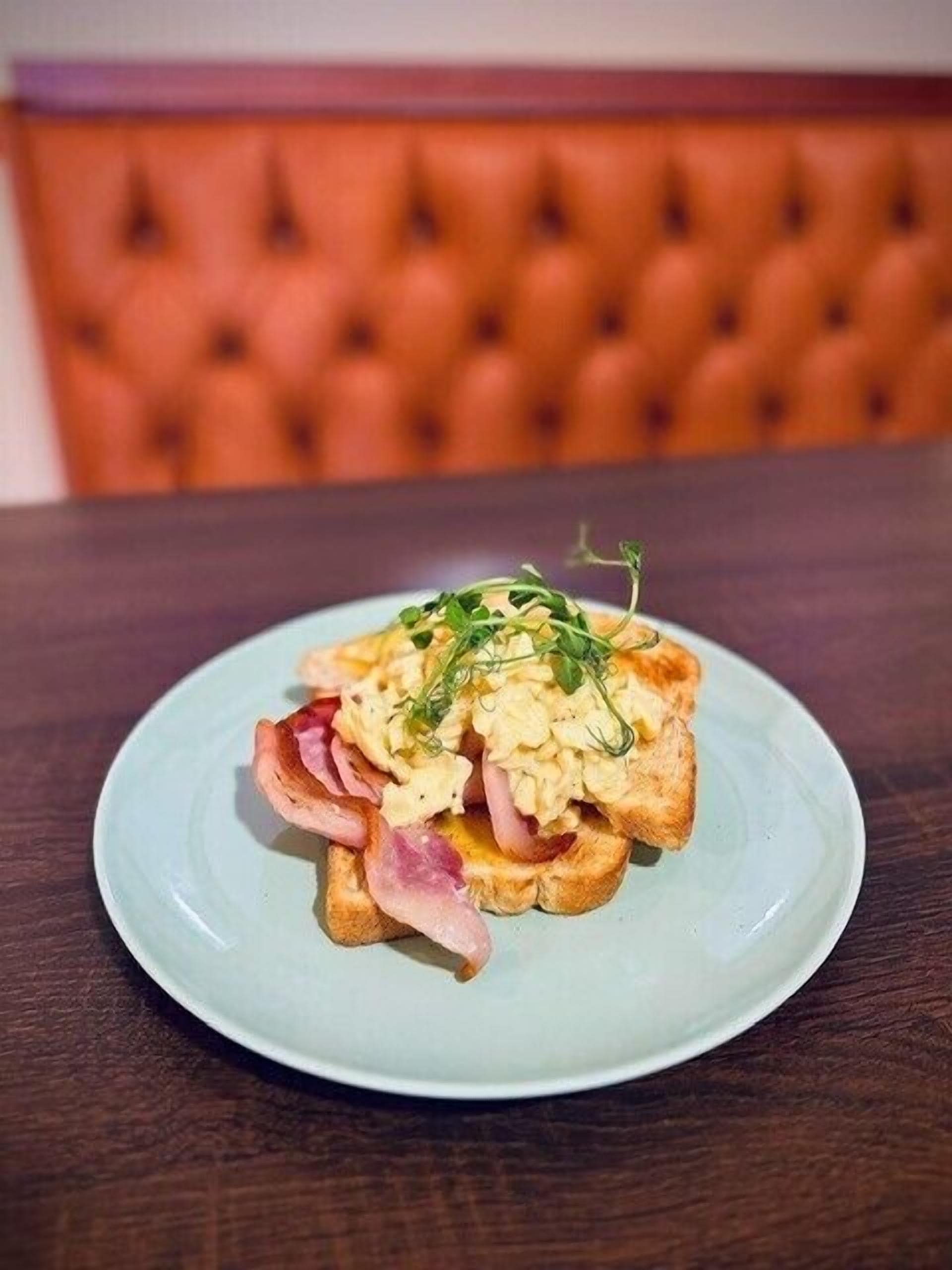 A plate of scrambled eggs on toast with ham and a sprig of greenery, placed on a light blue plate.
