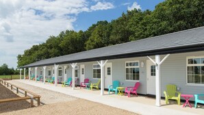 A row of colorful Adirondack chairs and tables outside a building with a covered porch. - Silverstone Golf Club & Hotel (Buckingham)