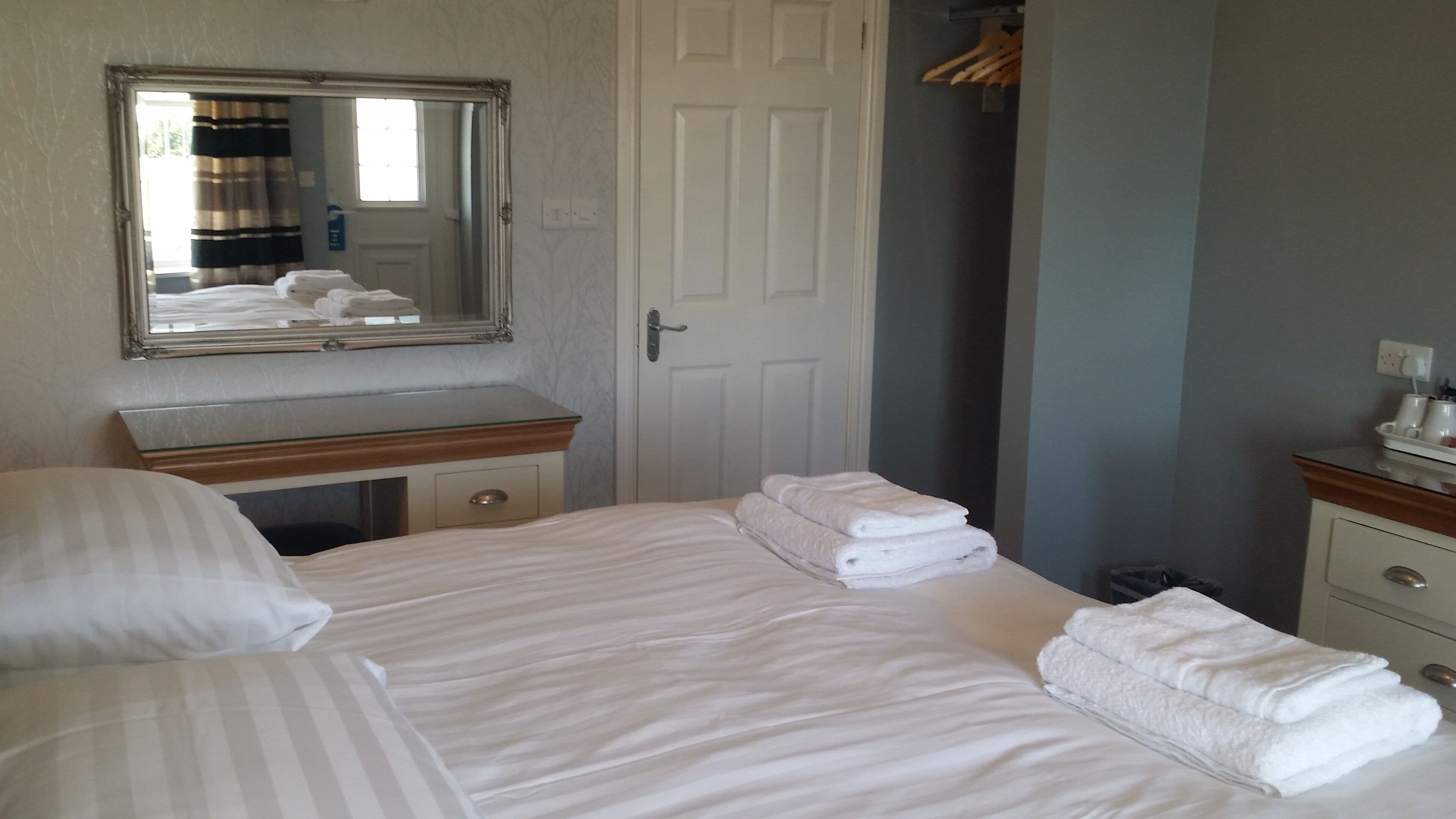 Une chambre d’hôtel avec un lit, une commode, un miroir et une porte.