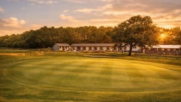 Un campo de golf con un club de campo y árboles al fondo.