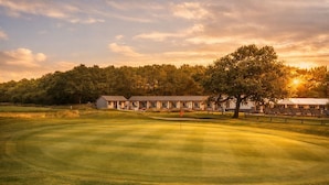 A golf course with a clubhouse and a large tree in the foreground. - Silverstone Golf Club & Hotel (Buckingham)