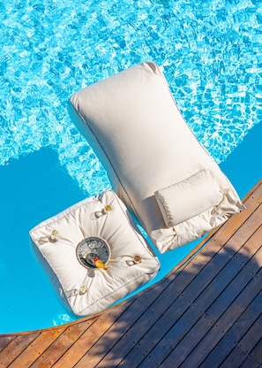 Två vita loungestolar med kuddar och flaskor med alkohol placerade vid en pool.