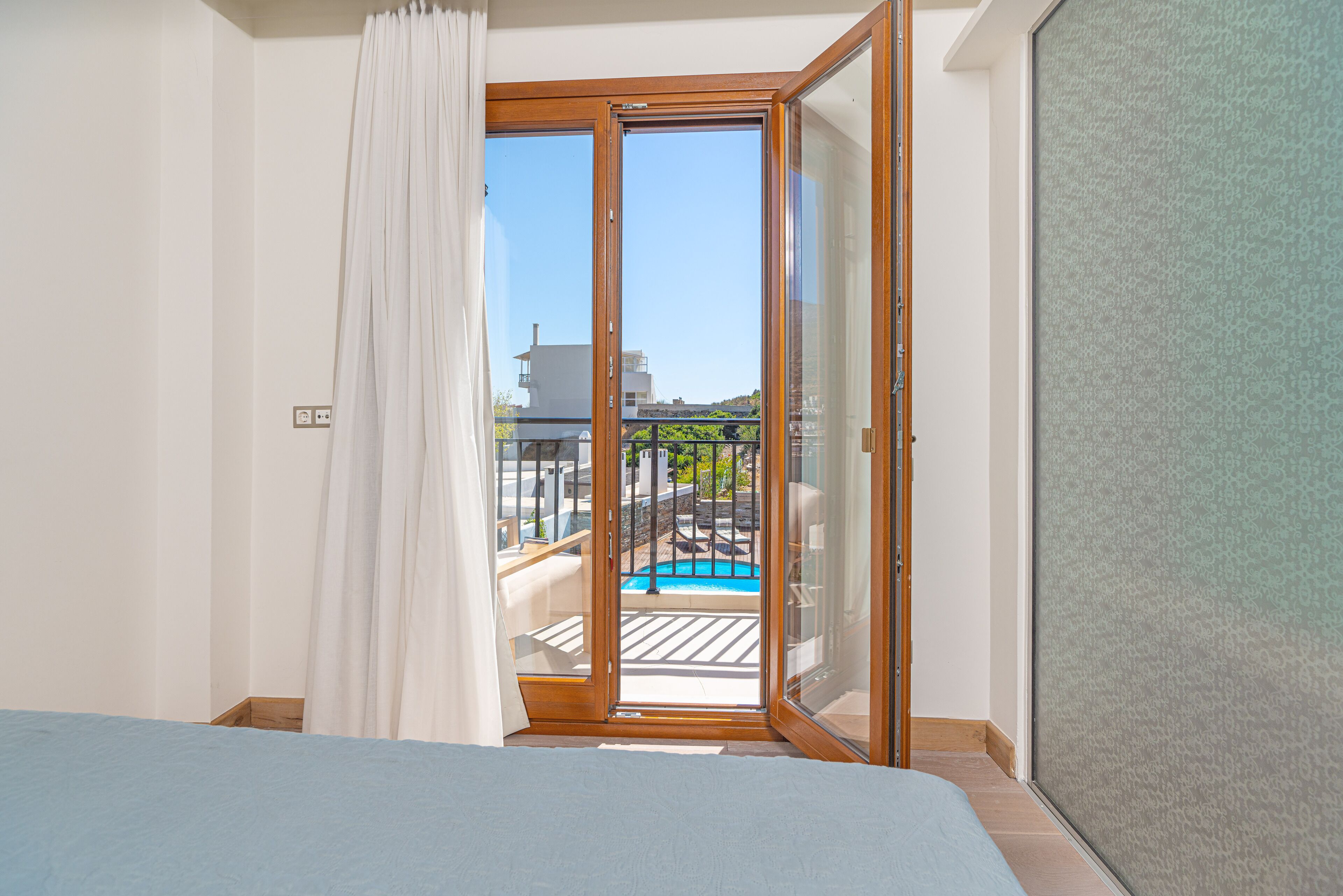 A hotel room with a bed, a sliding glass door leading to a balcony with a pool.