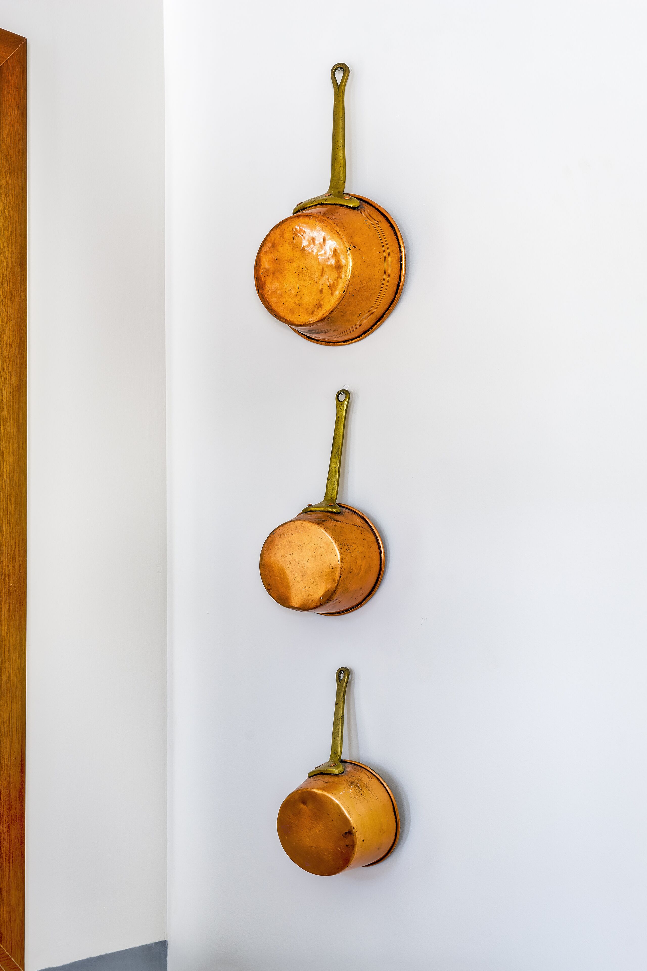 A wall-mounted set of three copper-colored pots.