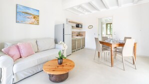 A modern living room with a white sofa, a wooden coffee table with a plant, and a dining area with a wooden table and chairs. - Belvedere Andros (Andros)