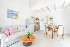 Ett modernt vardagsrum med en vit soffa, ett träbord som används som soffbord med en växt på, och en matplats med ett träbord och stolar.
