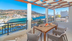 A balcony with a wooden table and wicker chairs, overlooking a coastal town and a bay. - Belvedere Andros (Andros)