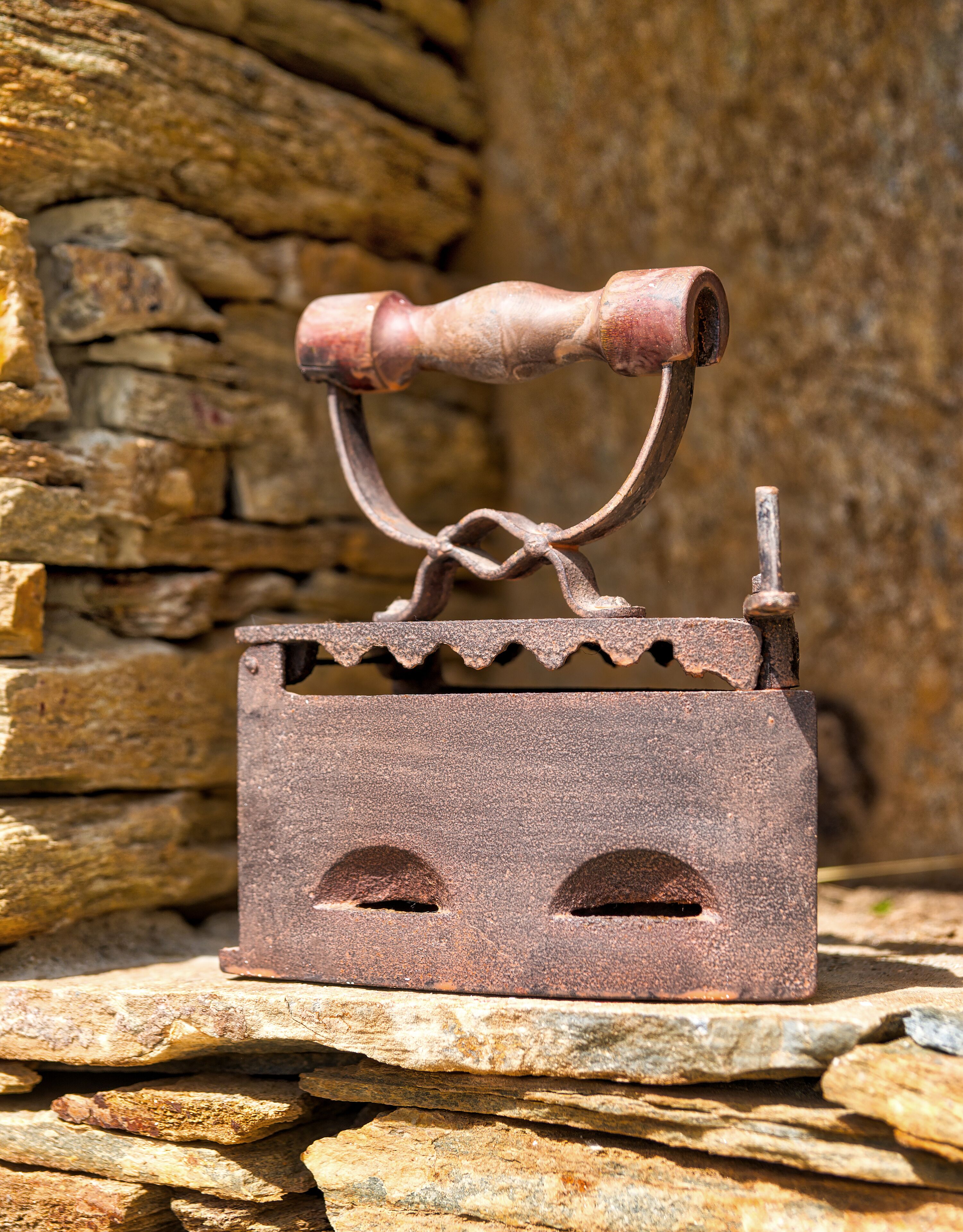 An antique iron with a wooden handle and a metal body, placed on a stone surface.