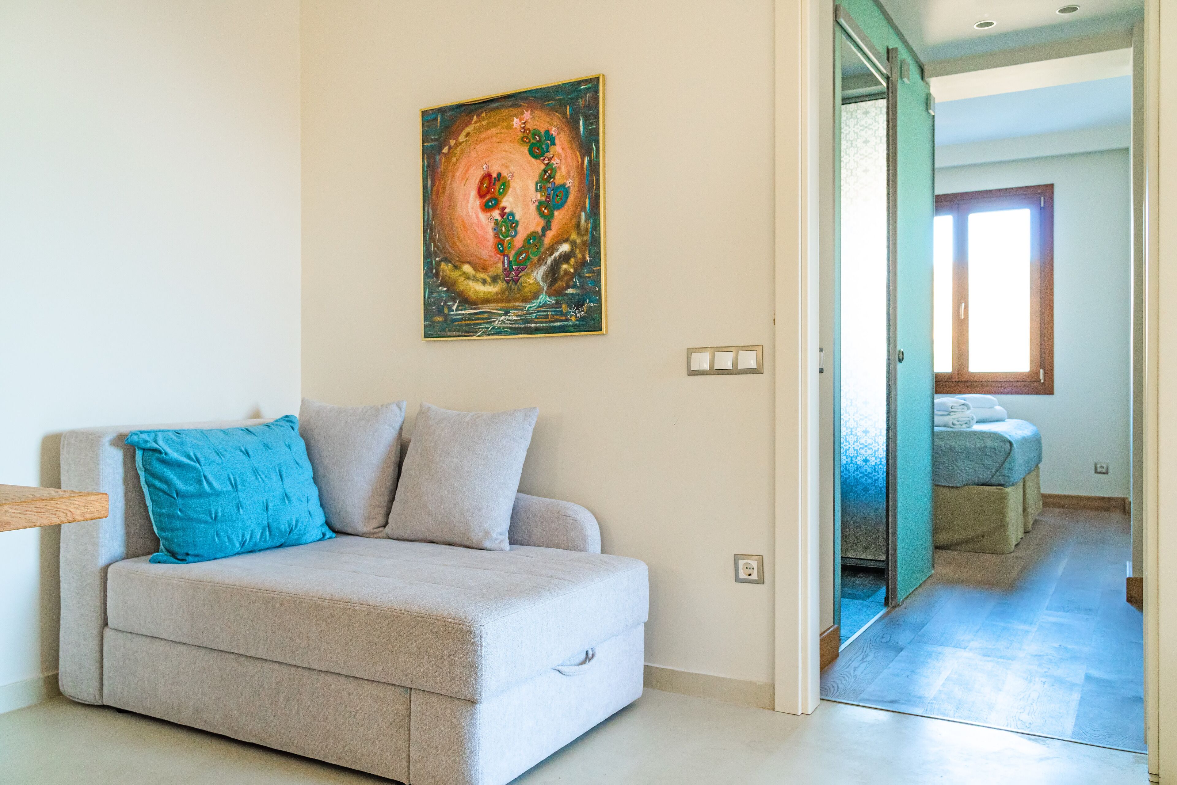 Ein Wohnzimmer mit einem beigen Sofa, einem blauen Kissen und einem Bild an der Wand.