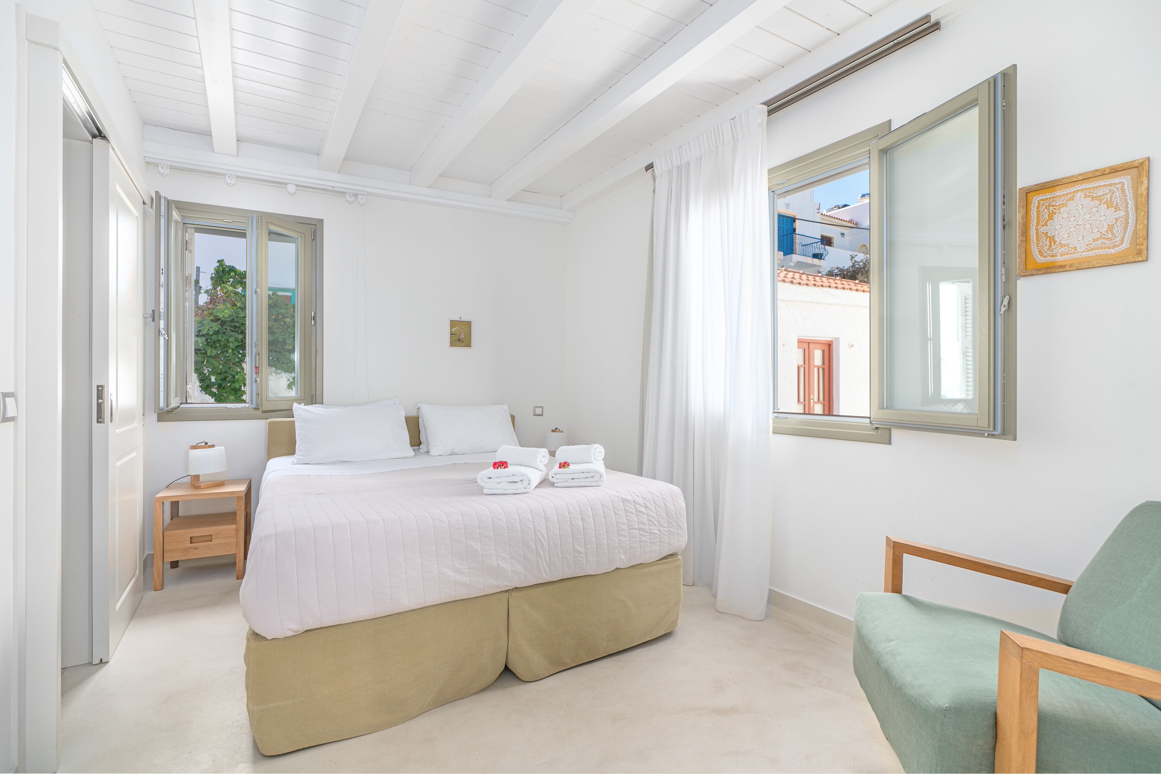 Una habitación de hotel con una cama grande, una mesita de noche con lámpara, una silla y una ventana con cortinas.