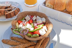 Un plato con ensalada de queso feta, tomates, pepinos y cebollas rojas, acompañado de pan y galletas.