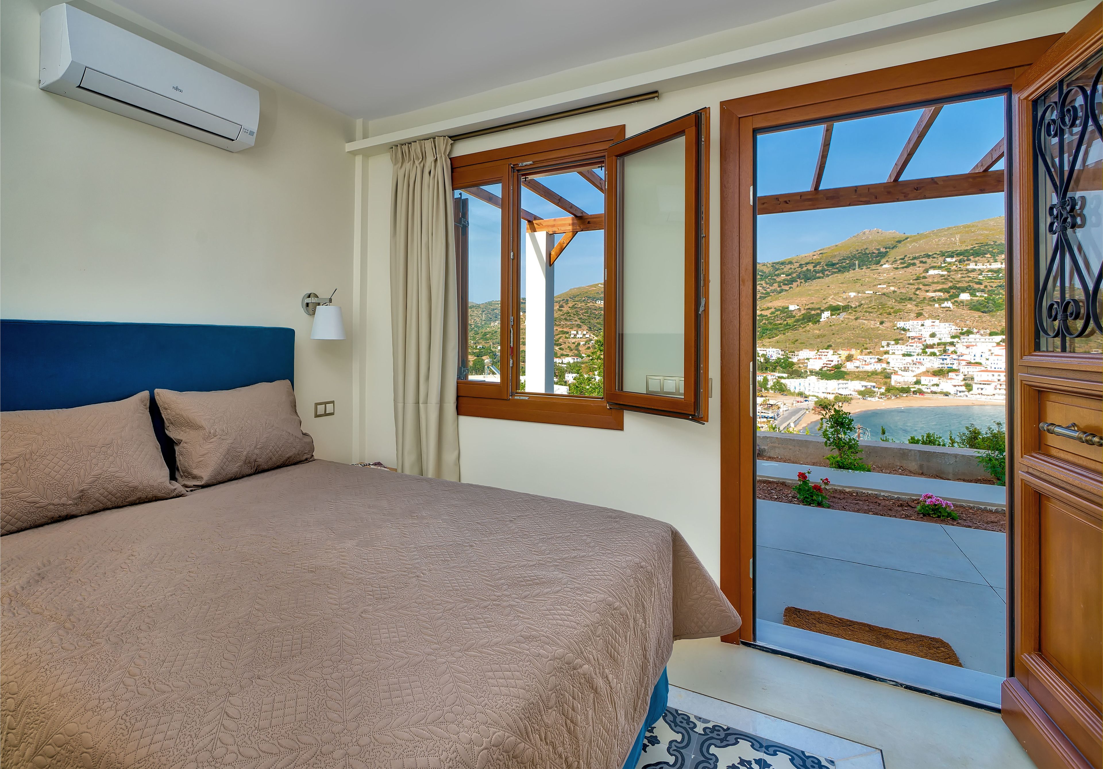 A bedroom with a bed, an air conditioner, a window, and a view of a coastal landscape.