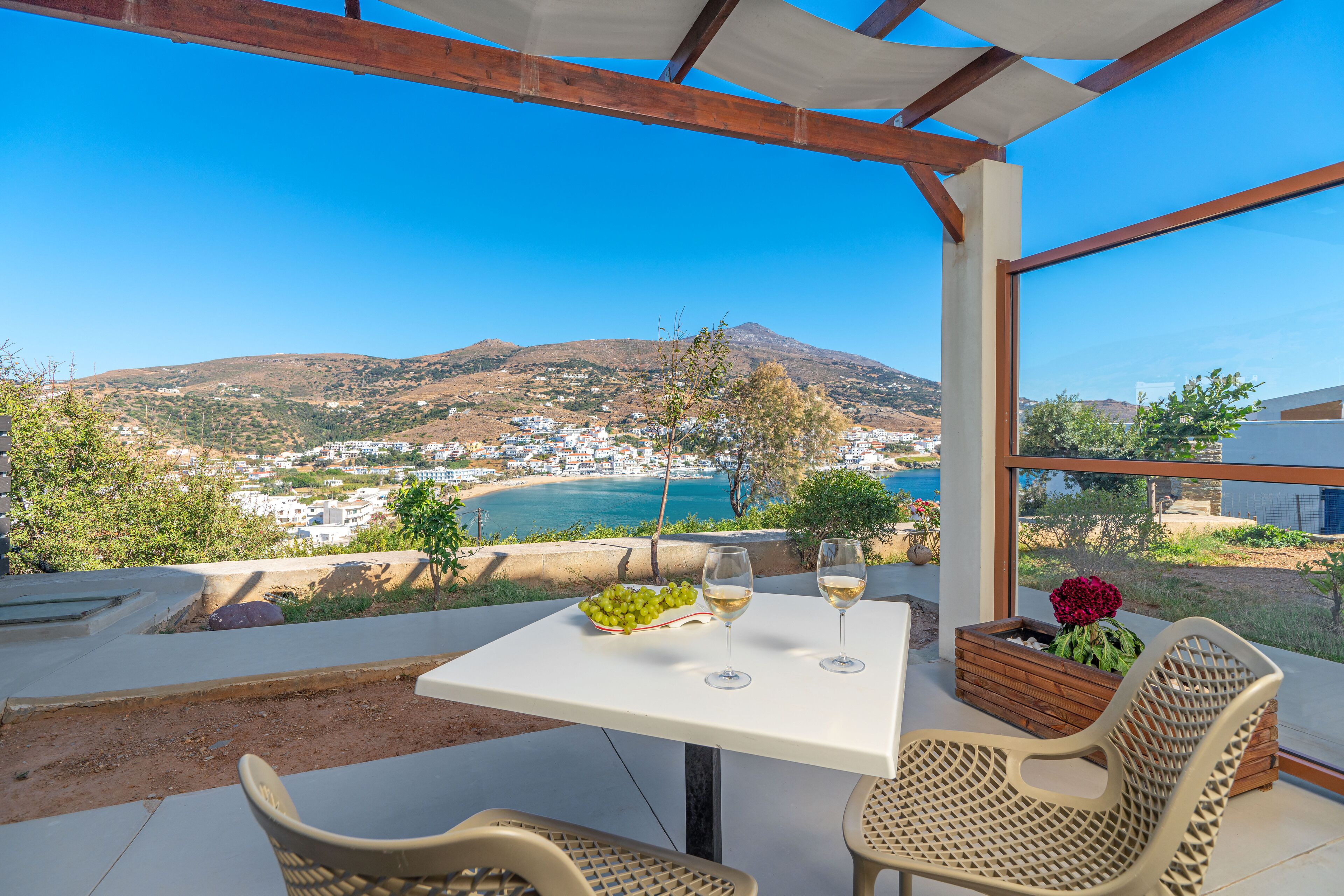 A terrace with a table, two chairs, and a view of a coastal town and mountains.