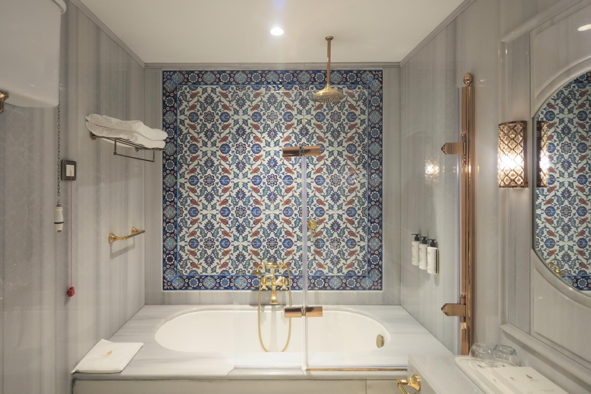 A modern bathroom with a freestanding bathtub, a shower with a golden showerhead, and a tiled wall with a geometric pattern.