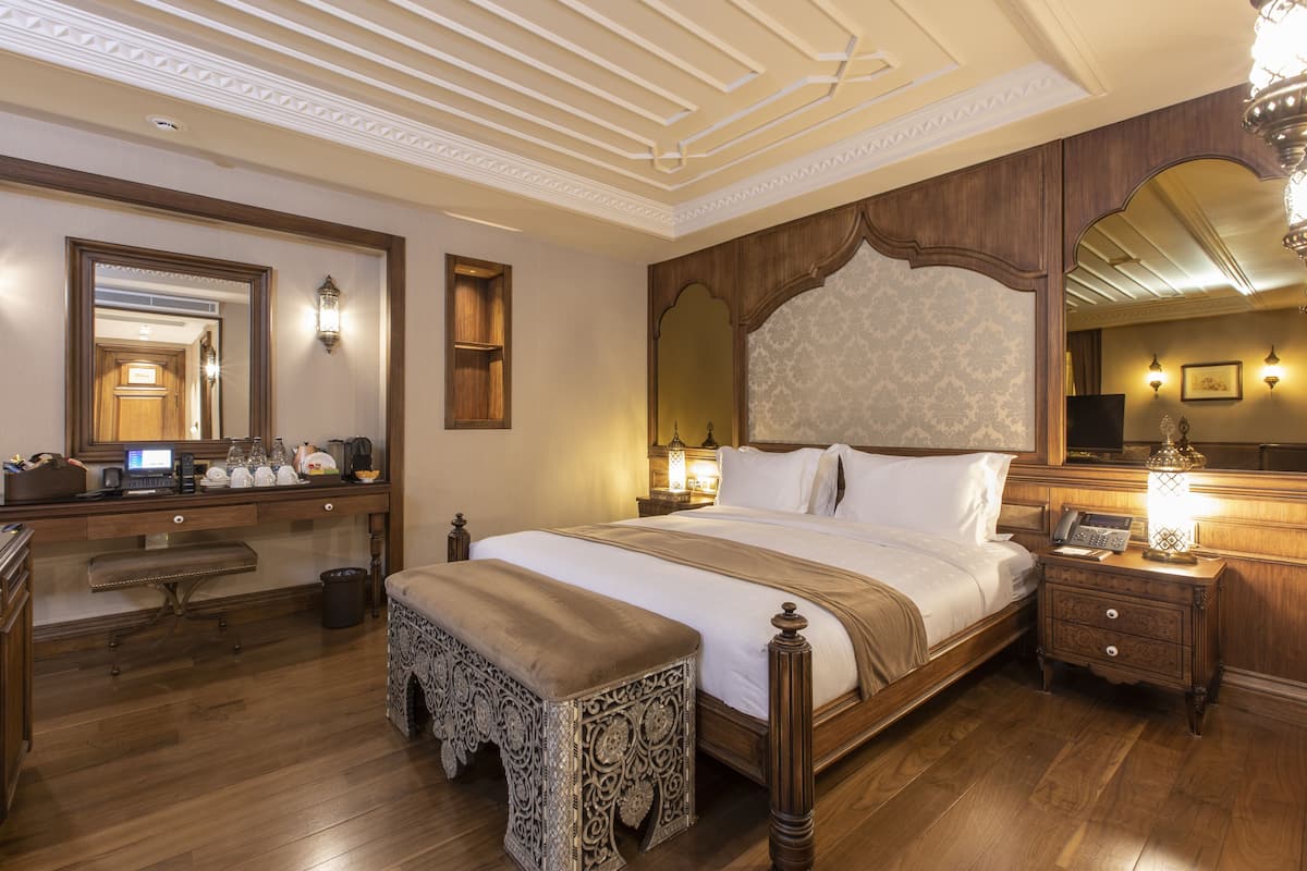 A spacious bedroom with a large bed, wooden headboard, and a nightstand with a lamp.