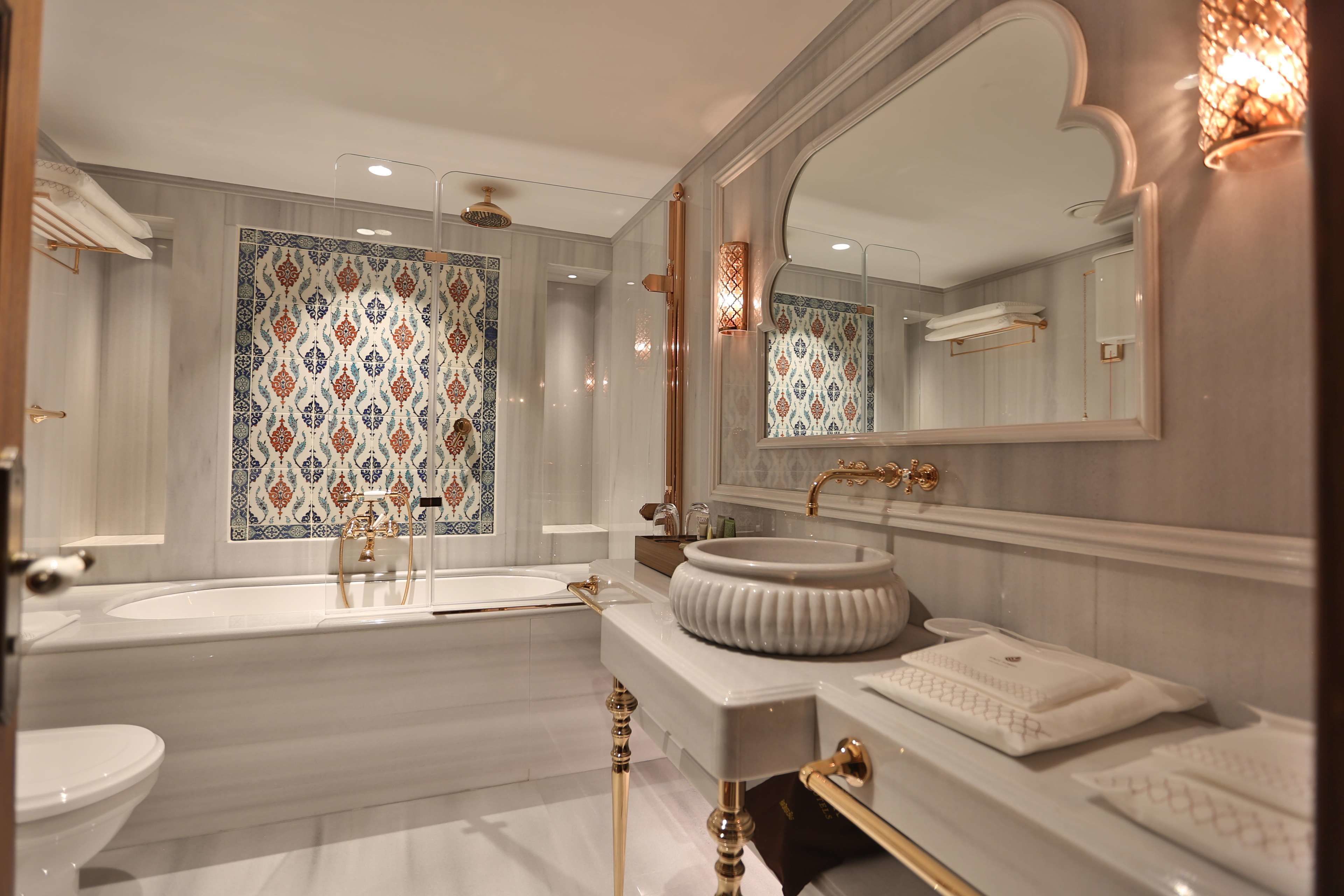 A luxurious bathroom with a large bathtub, a round sink, and a mirror with a decorative frame.