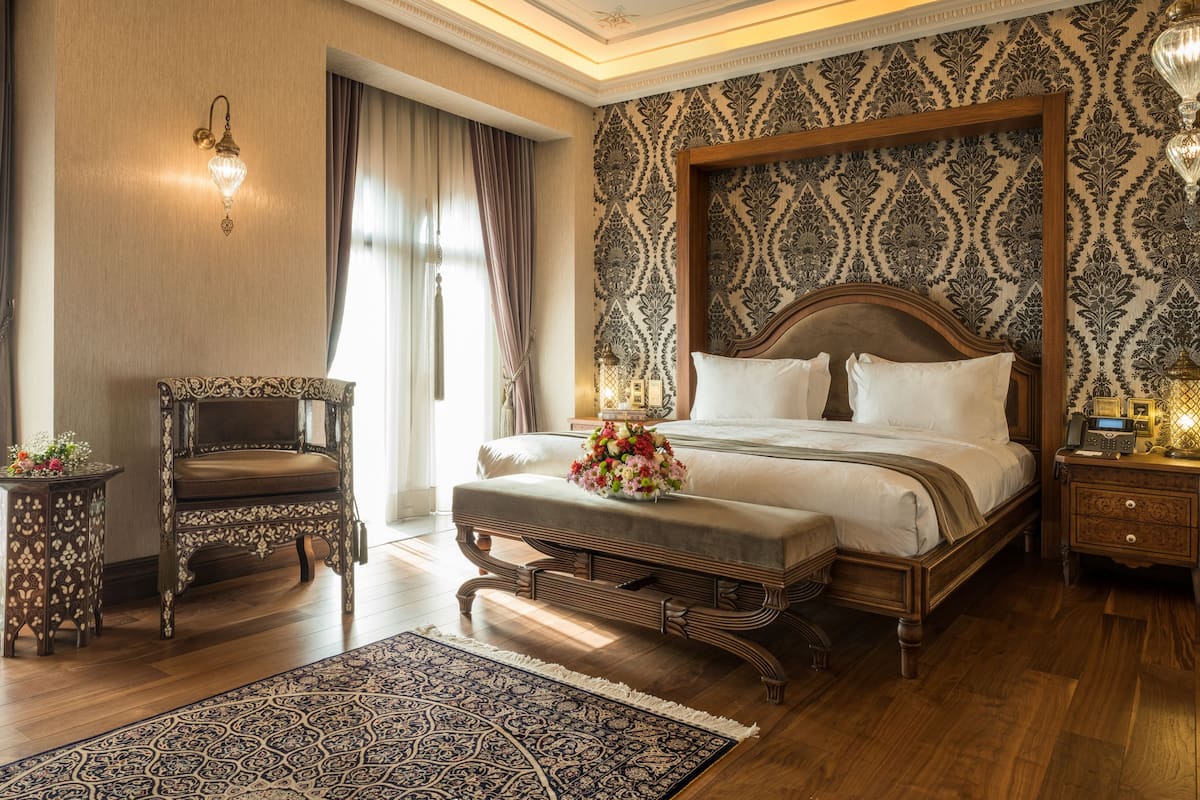 A bedroom with a large bed, a wooden nightstand, a chair, and a patterned rug.