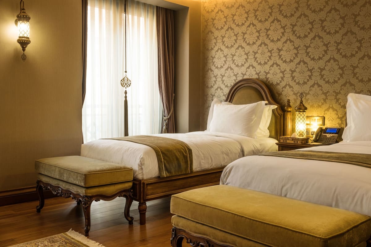 A hotel room with two beds, a nightstand with a lamp, and a wooden floor.