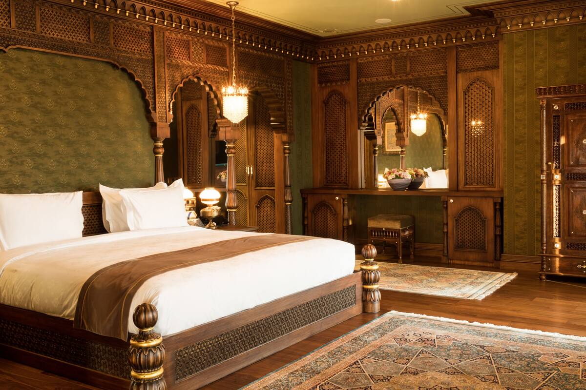 A large, ornate bed with a wooden headboard and footboard, flanked by two nightstands with lamps.