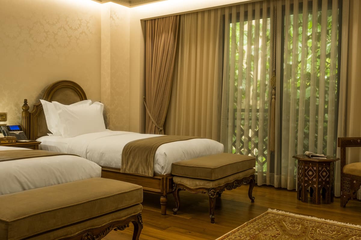 A hotel room with a large bed, two bedside tables, a small side table, and a wooden chair.