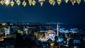 A restaurant with a table set for dining, a view of a cityscape, and hanging decorative lights. - AJWA Sultanahmet (Istanbul)