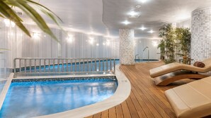 A modern indoor pool area with a curved pool, lounge chairs, and potted plants. - AJWA Sultanahmet (Istanbul)
