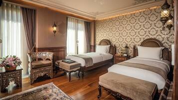 A hotel room with two beds, a sitting area with a chair and table, a decorative rug, and a patterned wallpaper.