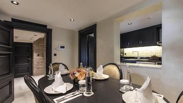 Un comedor con una mesa de madera oscura dispuesta para cuatro personas, rodeada de sillas de madera oscura. Hay un centro de mesa decorativo y se ve una cocina moderna a través de un arco.